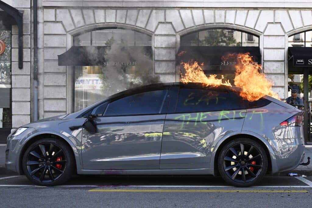 Cette photographie montre une Tesla en feu, sur laquelle est inscrit le message &laquo; &Agrave; bas les riches &raquo;, lors d'un rassemblement de la coalition &laquo; Non au G7 &raquo;, regroupant plus de 60 associations, syndicats et groupes de gauche &laquo; contre le fascisme et l'imp&eacute;rialisme &raquo;, la veille du sommet, &agrave; Gen&egrave;ve le 14 juin 2026