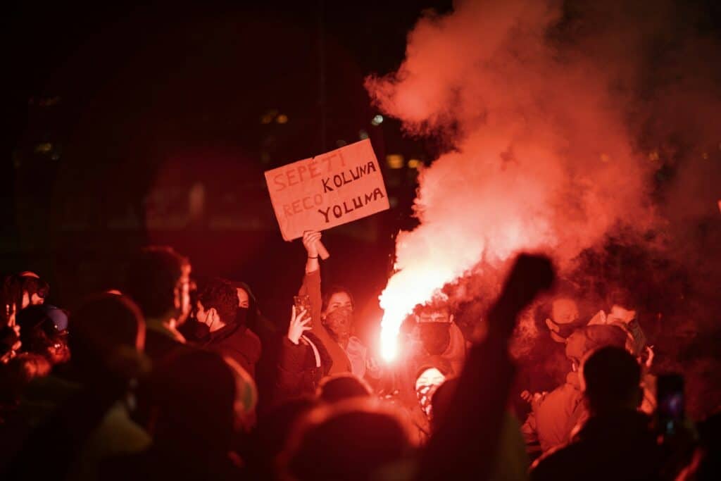 Protestors rally with flares and signs at night.